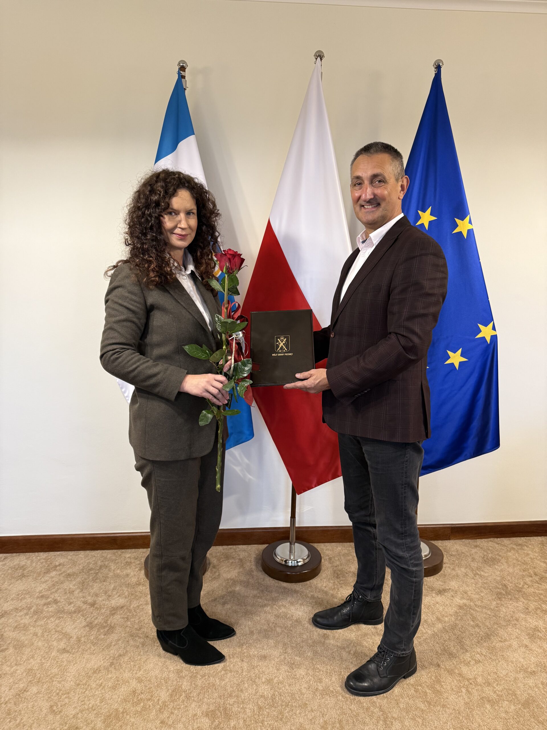 Na fotografii wójt oraz pani dyrektor Agnieszka Klugiewicz, która pozuje z różą. W tle flagi: Polski, Unii Europejskiej oraz flaga z herbem gminy Przemęt.