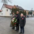 Na fotografii Janusz Frąckowiak, Wójt Gminy Przemęt, Robert Szwed, Prezes Towarzystwa Pamięci Powstania Wielkopolskiego – Koło w Przemęcie, oraz Antoni Fornalski, Honorowy Prezes Towarzystwa. Wójt Janusz Frąckowiak trzyma wiązankę, pan Robert i pan Antoni stoją obok. Wszyscy oddają hołd powstańcom przy pomniku na przemęckim rynku.