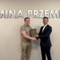 Na fotografii widoczny jest zastępca wójta i wykonawca, którzy pozują do zdjęcia z umową. W tle srebrny napis: "Gmina Przemęt".